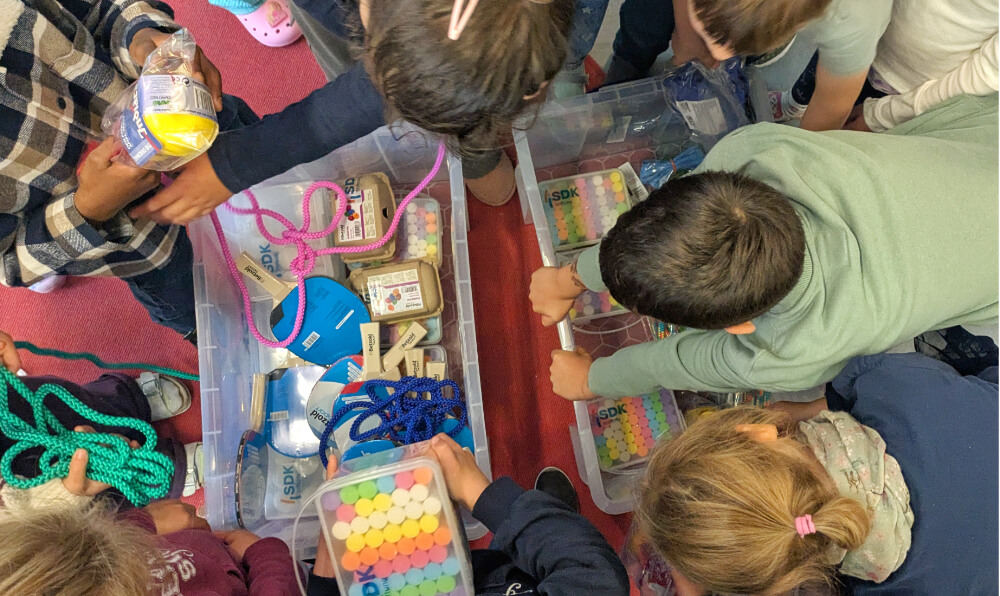 Kinder die Boxen mit Bewegungsmateraline öffnen, wie Sprinseile, Kreide, Tischtennisschläger
